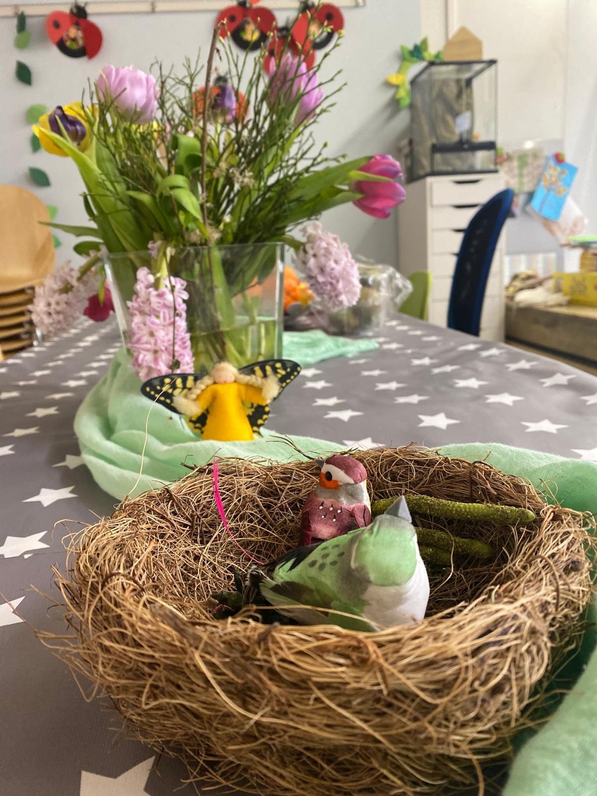 Vogelnest mit kleinen Vögeln auf dem Tisch, dahinter Tulpen und Hyazinthen
